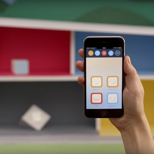 A hand holding a mobile phone with an app that shows the air quality as measured by IoT devices blurred in the background.